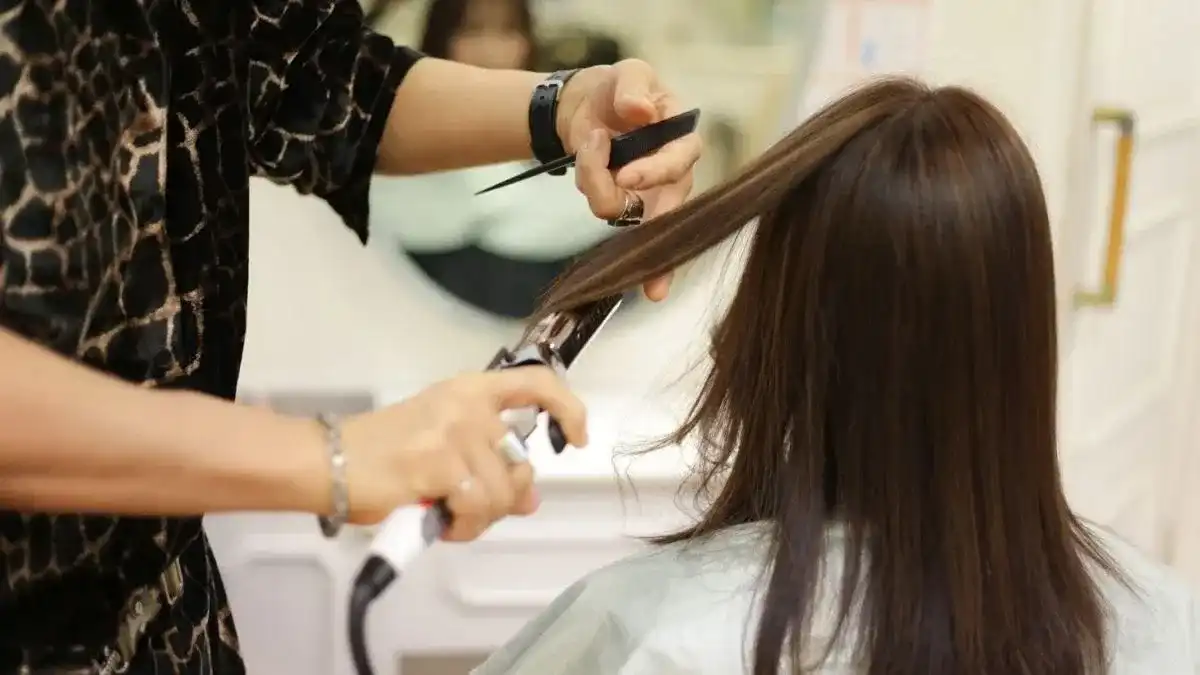 Hairdresser styling a woman's hair with a flat iron in a salon setting.