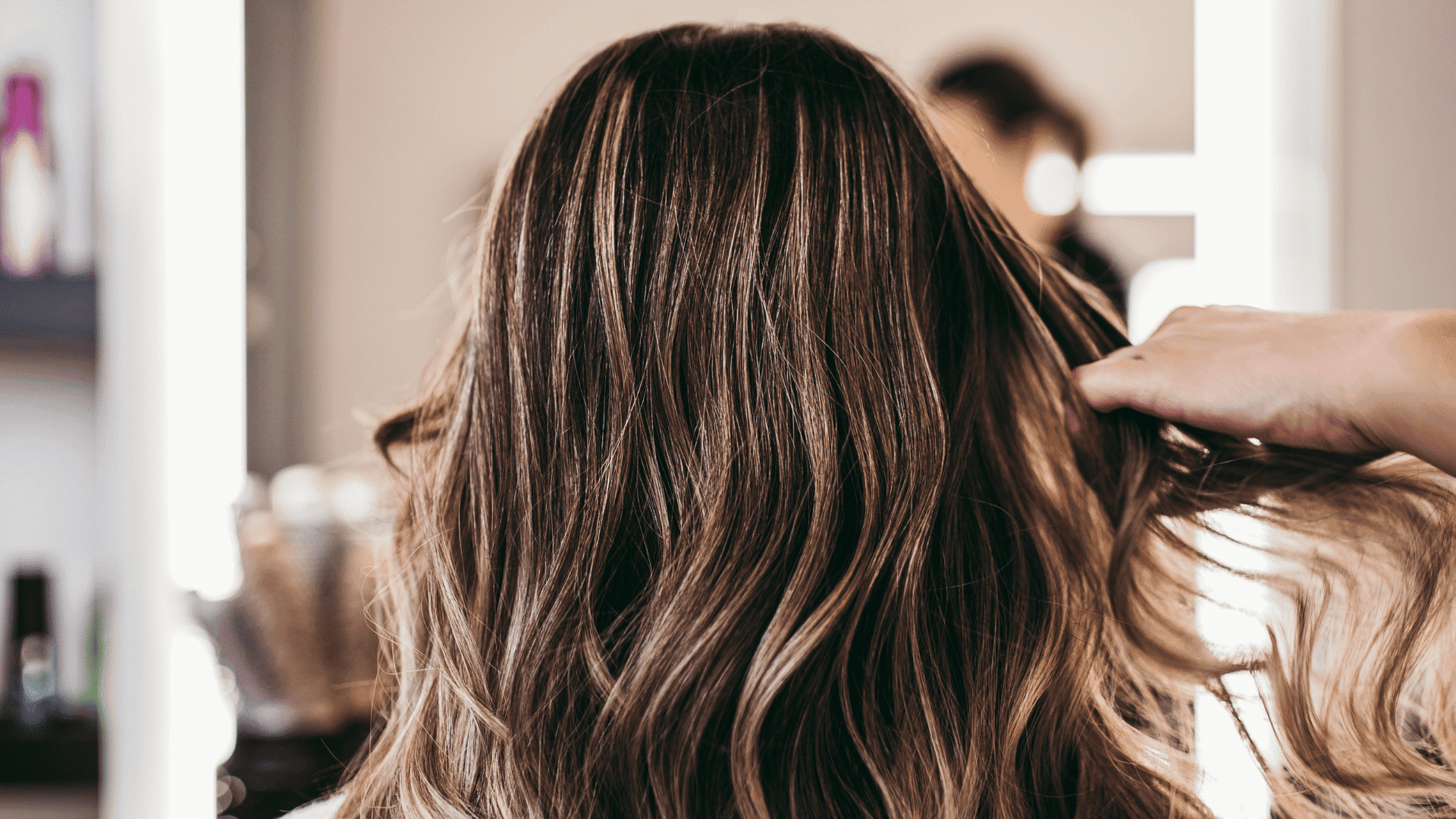 Hairdresser styling long, brown hair with highlights at a salon.