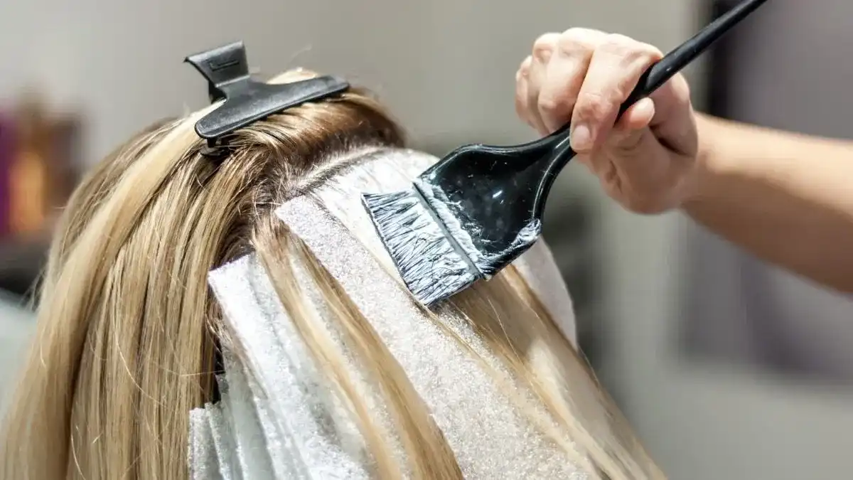 Hair coloring process with brush applying dye on blonde hair with foil.